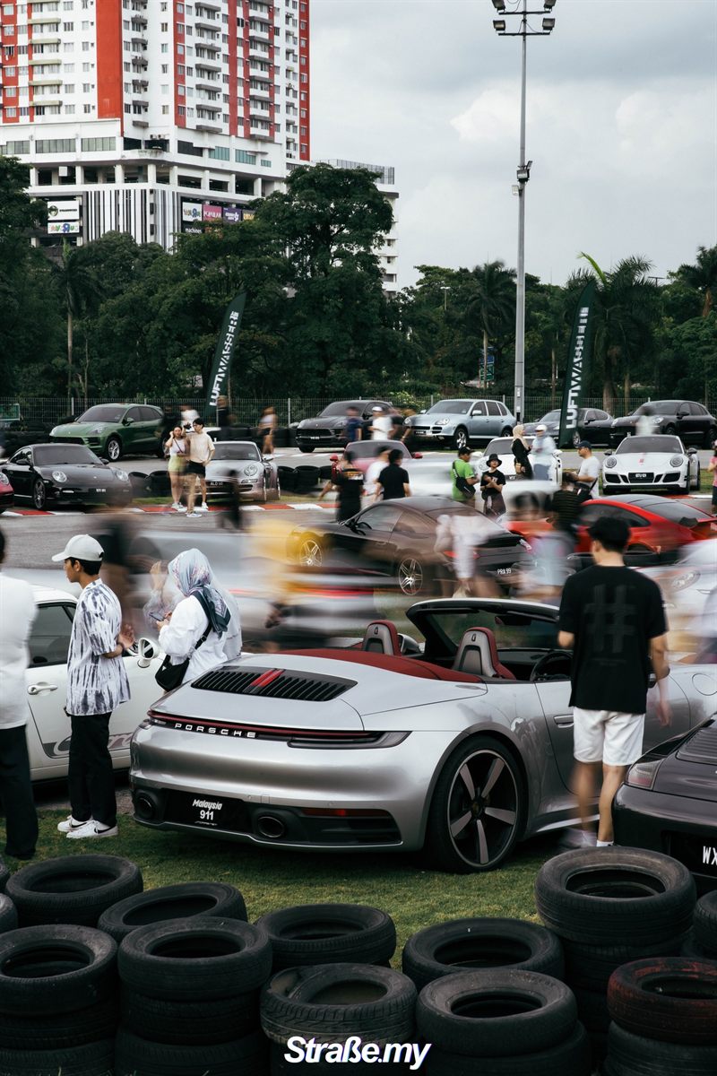 Silver 992 cabriolet on the grass as the crowd streams past